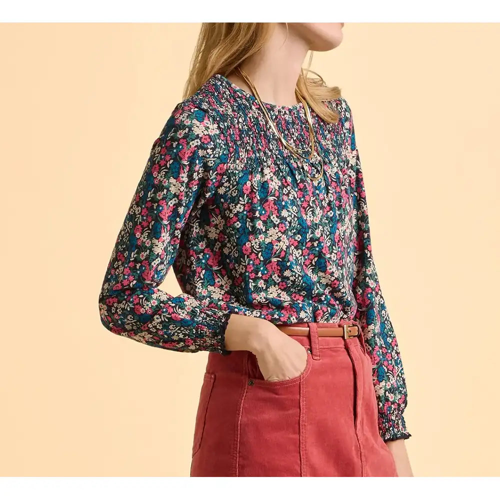 Person wearing a floral blouse and red pants on a beige background