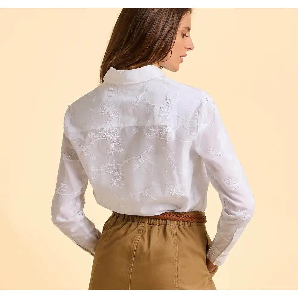 Woman wearing a white embroidered blouse and brown pants on a beige background