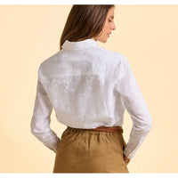 Woman wearing a white embroidered blouse and brown pants on a beige background