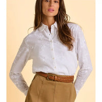 Woman wearing a white embroidered shirt and beige pants against a beige background