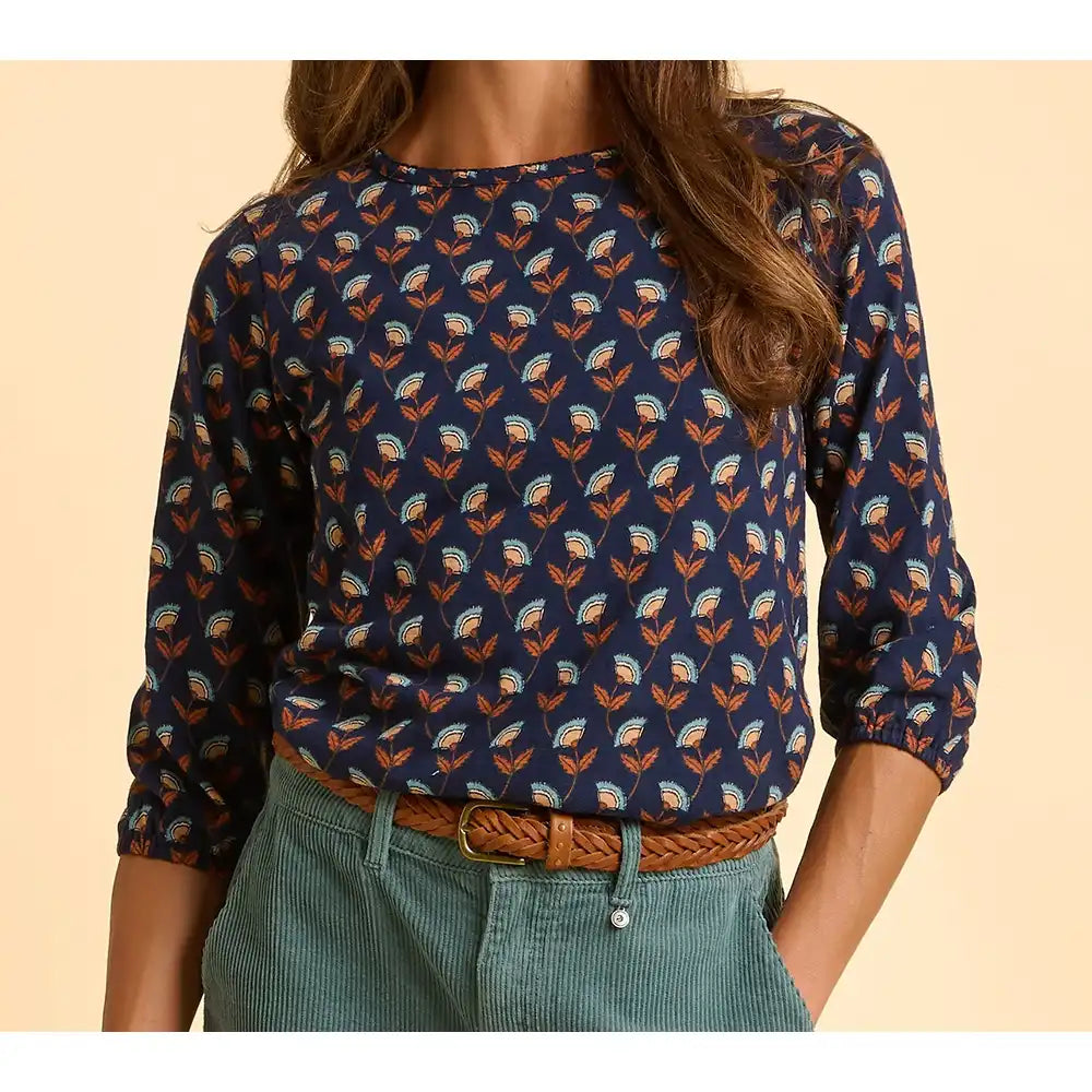 Person wearing a navy blue floral patterned shirt with rolled-up sleeves on a beige background