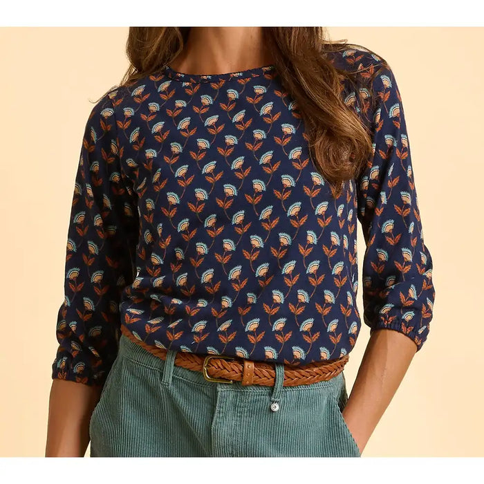 Person wearing a navy blue floral patterned shirt with rolled-up sleeves on a beige background