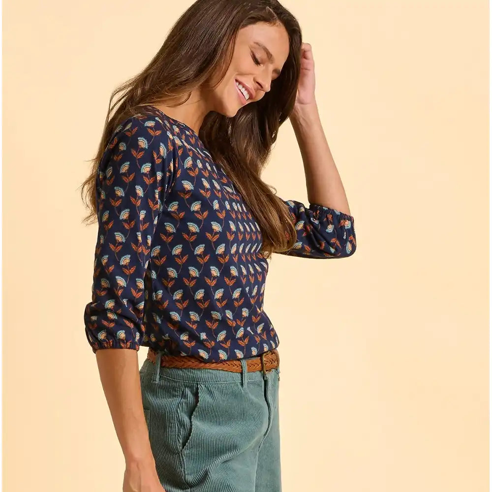 Woman wearing a patterned blouse and green pants on a beige background