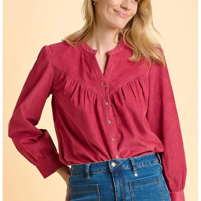 Woman wearing a red blouse with long sleeves and blue jeans on a beige background
