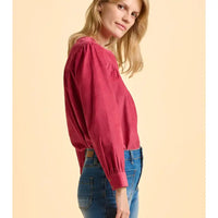Woman wearing a red blouse and blue jeans against a beige background