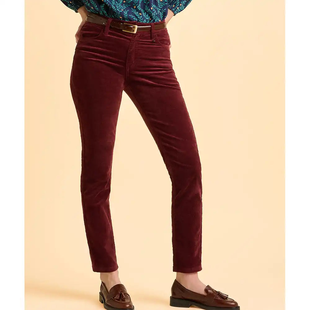 Maroon velvet pants worn by a person on a beige background