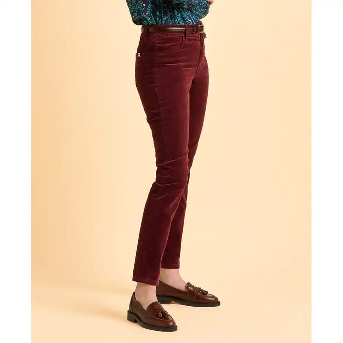 Maroon velvet pants worn by a person on a beige background