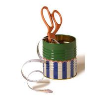 Green tin can with striped design, copper scissors, and a measuring tape on a white background