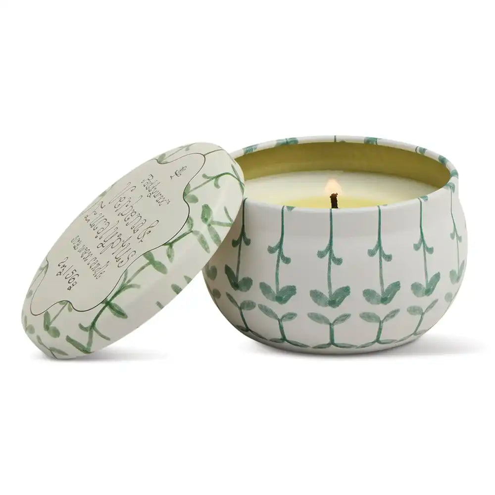 Candle in a decorative tin with leaf pattern on a white background