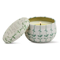 Candle in a decorative tin with leaf pattern on a white background