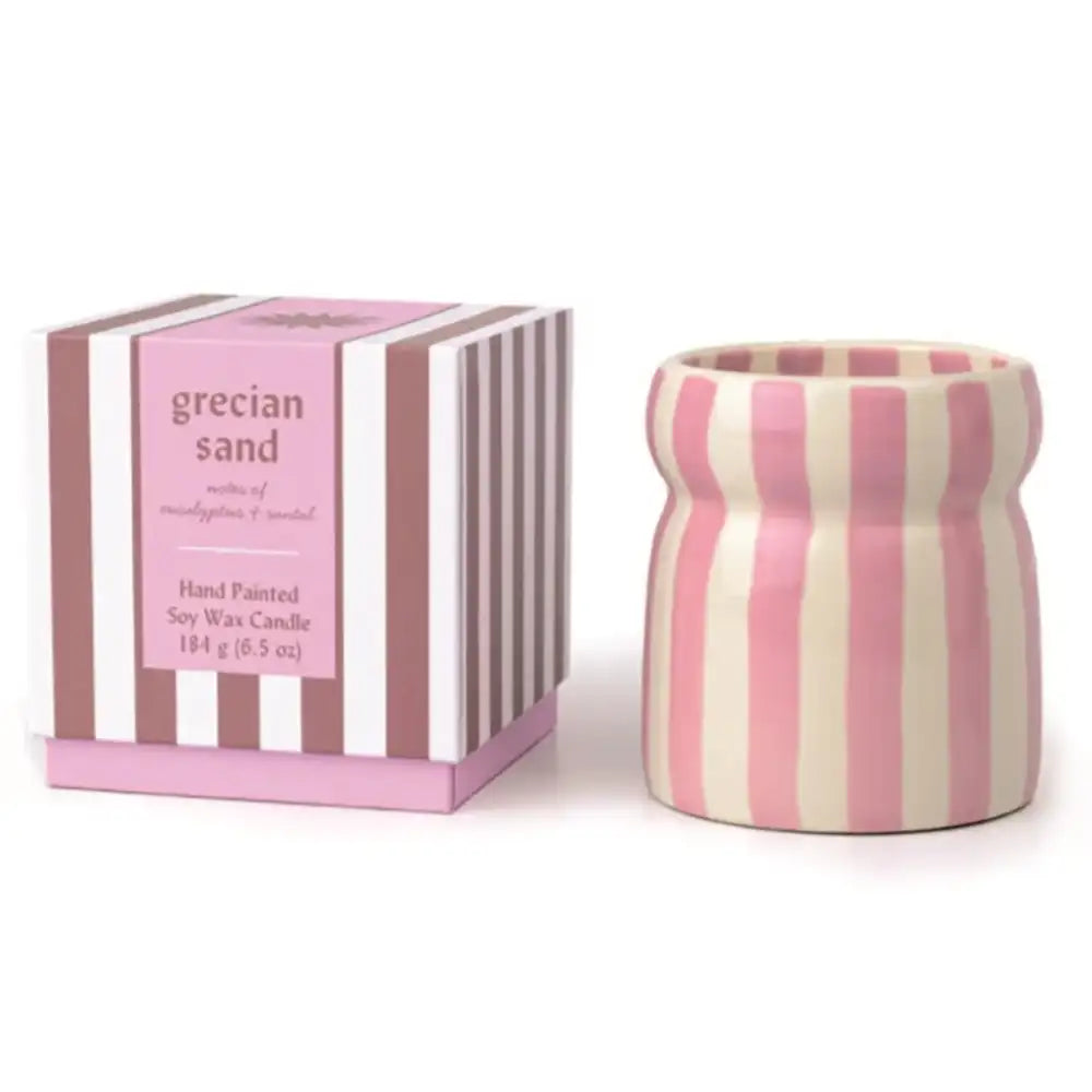 A pink and cream striped ceramic candle holder next to its matching striped packaging box, labeled 'grecian sand' scented soy wax candle.