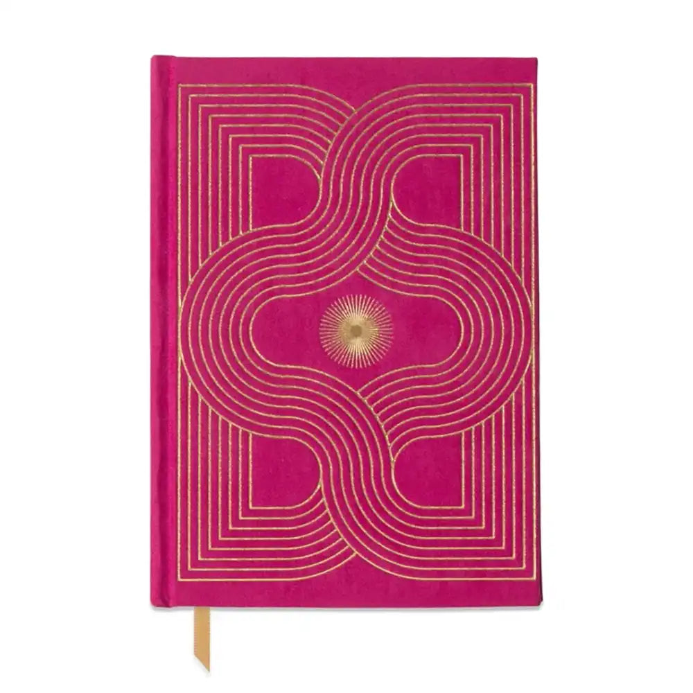 A bright pink hardcover notebook with a gold geometric pattern and a small gold sunburst emblem on the cover, featuring a gold ribbon bookmark.