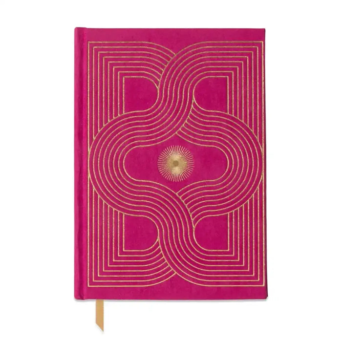 A bright pink hardcover notebook with a gold geometric pattern and a small gold sunburst emblem on the cover, featuring a gold ribbon bookmark.
