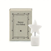 Match box gift box in the background with 'Happy Birthday' on the front. White porcelain square with metal wire that leads to a star on top. 