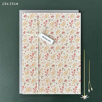 Pale ecru coloured card with delicate floral pattern in mustards, pinks and greens. White string down the left hand side tied into a bow with a white porcelain tag. Porcelain tag with black delicate writing with the words 'Birthday Girl'. 