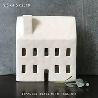 White ceramic house-shaped candle holder on a dark surface with a gray background