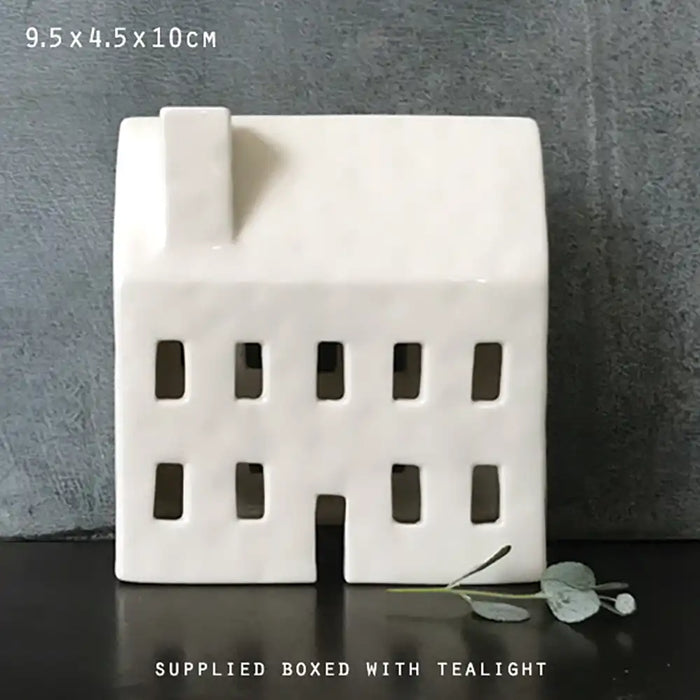 White ceramic house-shaped candle holder on a dark surface with a gray background