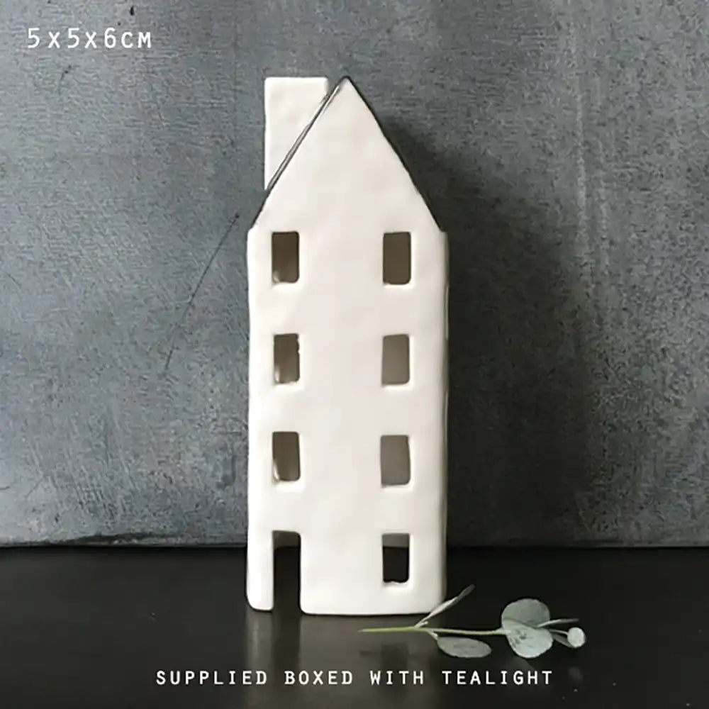 Ceramic house-shaped tealight holder on a dark surface with a gray background