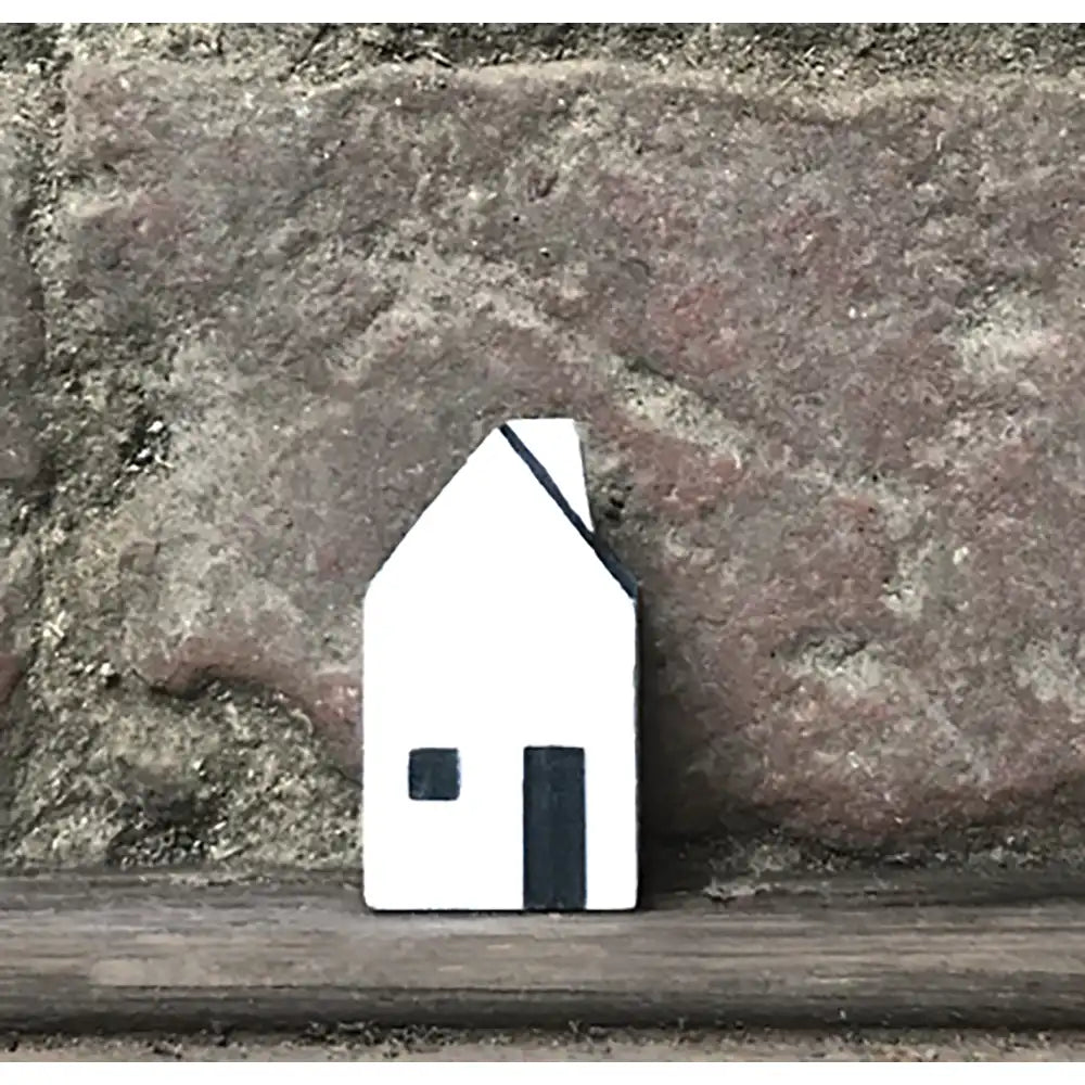 Small white house-shaped object on a wooden surface with a stone wall background