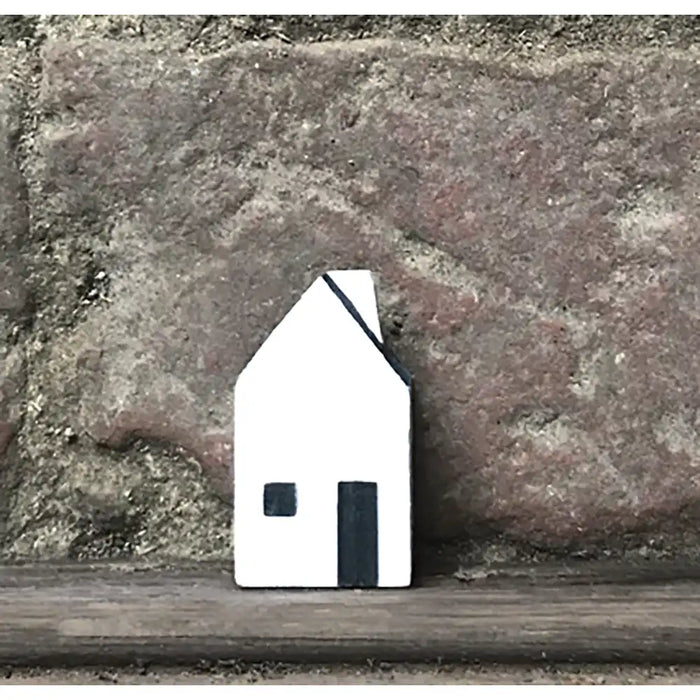 Small white house-shaped object on a wooden surface with a stone wall background