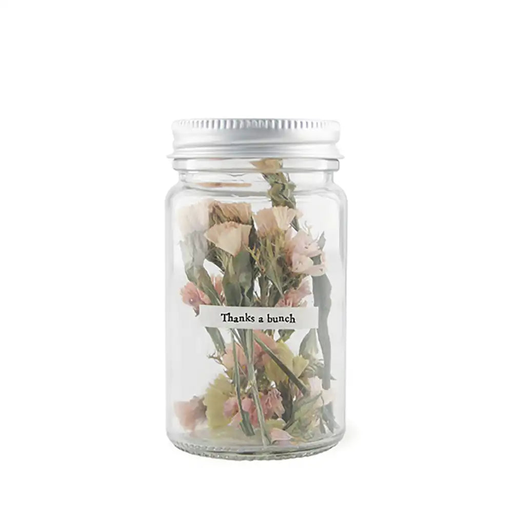 Glass jar with a silver lid. Jar contains dried flowers with white and pale pink. Jar has a small label over the front that says 'Thanks a bunch'.