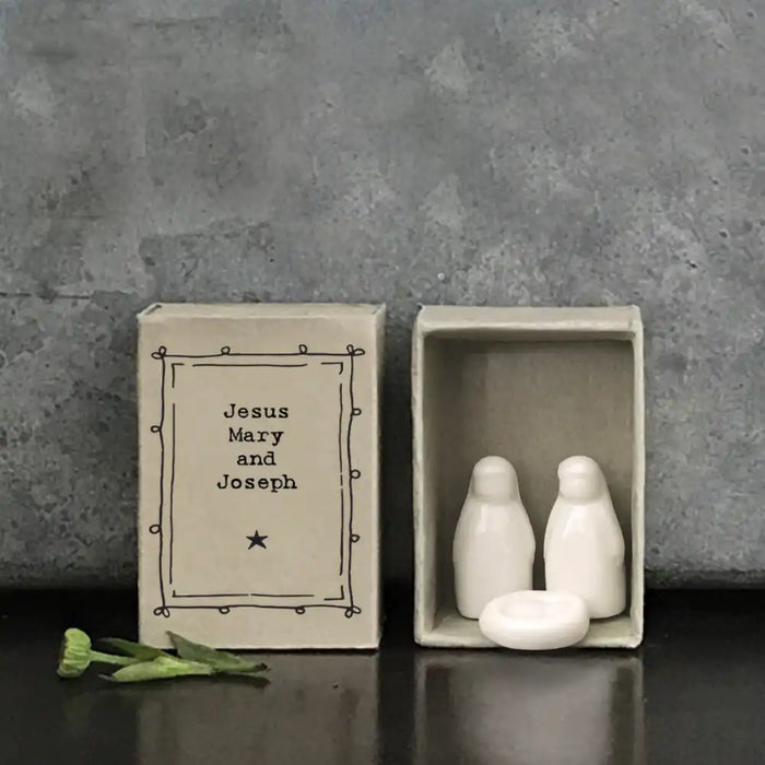 East of India matchbox containing white porcelain figures of Mary, Joseph and the baby Jesus. Against a granite background.