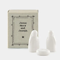 East of India matchbox with white porcelain figures of Mary, Joseph and the baby Jesus. Against a white background.