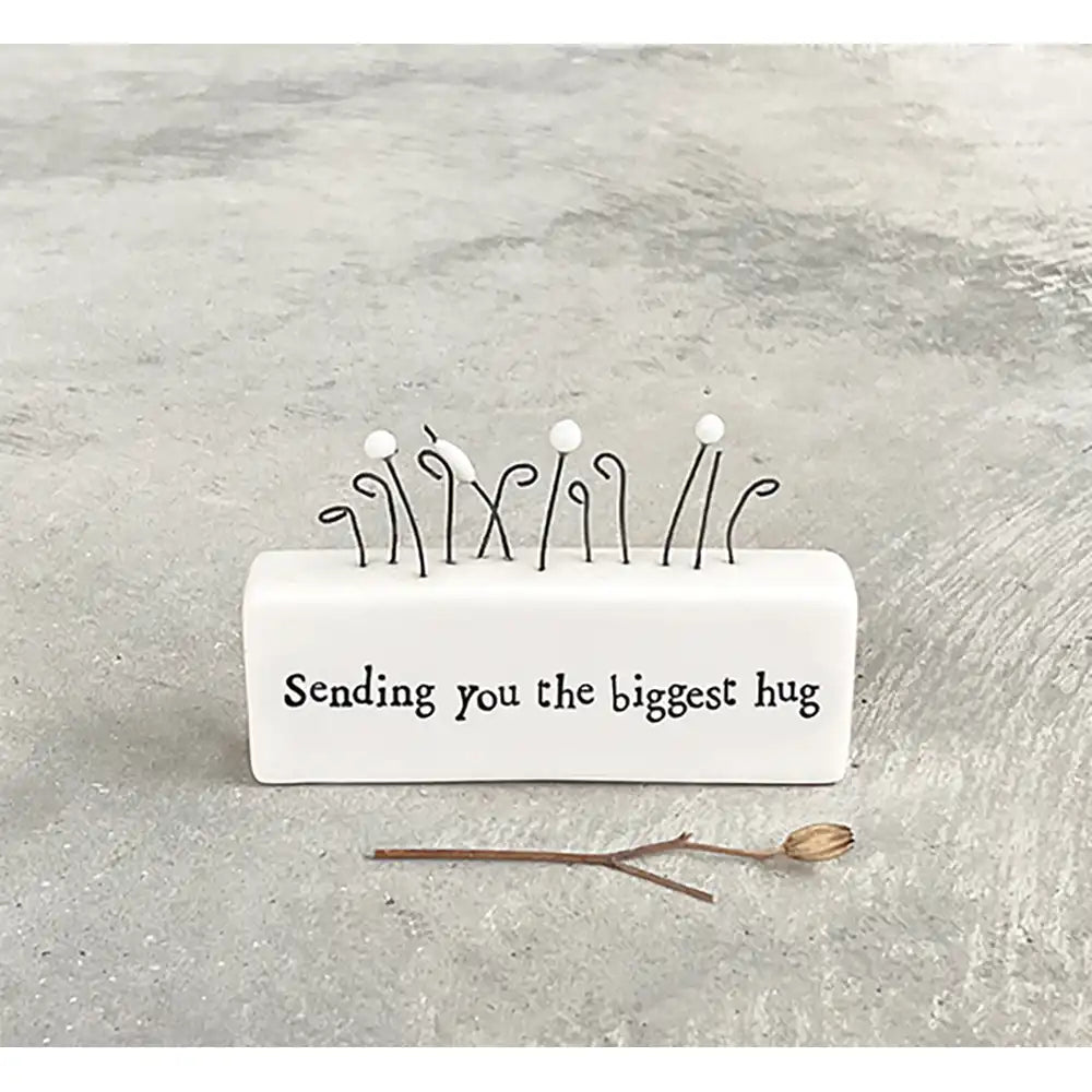 White porcelain rectangle with wire flowers on top. A saying in black on the front 'sending you the biggest hug'. 