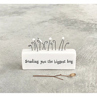 White porcelain rectangle with wire flowers on top. A saying in black on the front 'sending you the biggest hug'. 