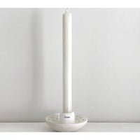 White candle holder with a white candle on a light gray background