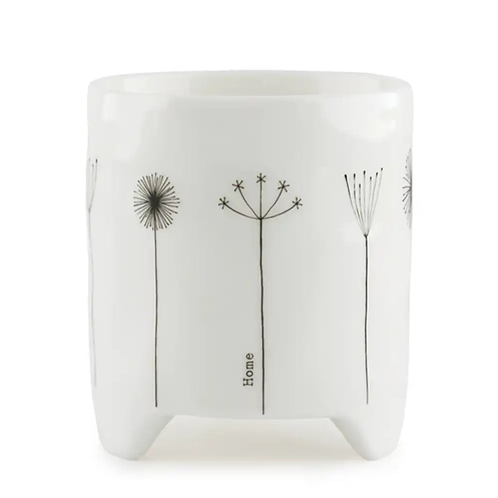 Gift box in background. White porcelain planter with black line flowers on he front and the word 'home' vertically in small text.