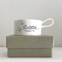 White mug with 'Snuggle up' text and design on a gray box against a light gray background