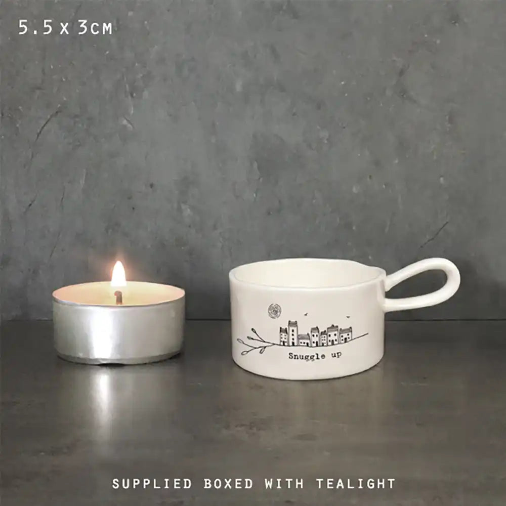 Small white mug with 'Snuggle' text and a lit tealight on a dark surface.
