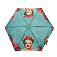 A hexagonal umbrella shown from above on a white background, featuring a teal-blue painted texture with printed portraits of Frida Kahlo wearing red flower crowns and red floral motifs along the edges.