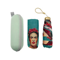 A set of three Frida Kahlo-themed accessories on a white background: a mint green hard case, a folded teal umbrella with a portrait print, and a matching rolled umbrella with a gold cap and tan loop.