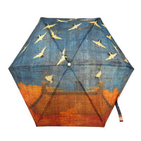 A hexagonal umbrella shown open against a white background, featuring a printed design of white cranes flying across a blue sky above an orange architectural landscape.