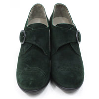 Fly London oil suede heeled shoes in pine green. Cross over strap with dark metal buckle. Decorative stitching over the toes. Front view.