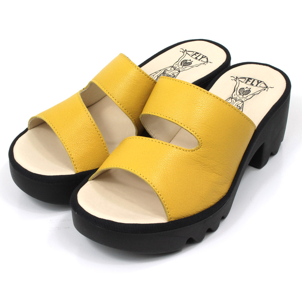 Fly London Mousse mule style sandals in yellow leather. Black chunky rubber heels and soles. Angled view