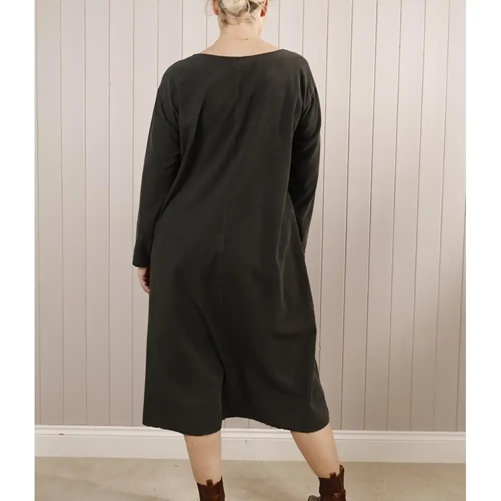 Person wearing a black dress standing against a wooden paneled wall.