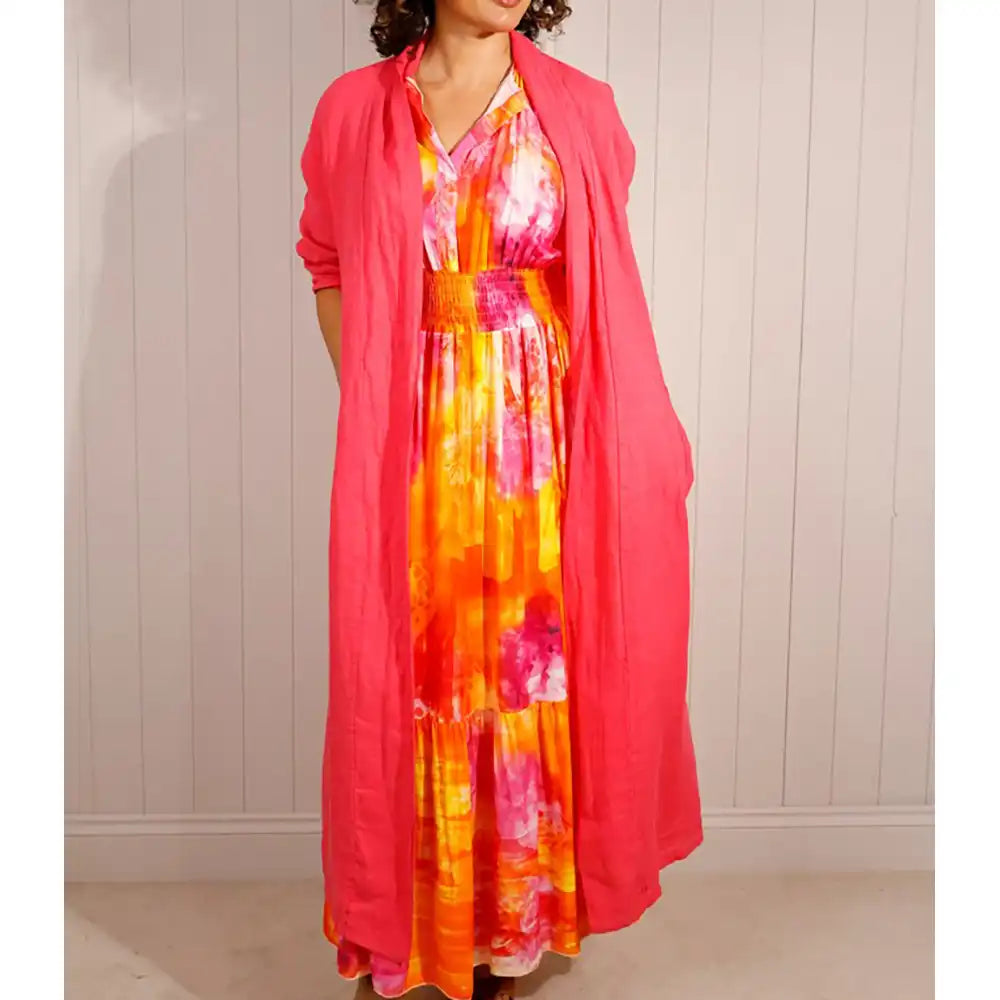 Woman wearing a colorful dress with a pink cardigan against a white wall.