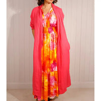 Woman wearing a colorful dress with a pink cardigan against a white wall.
