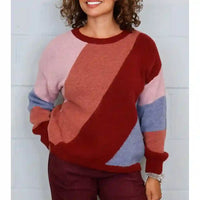 A woman wearing a fuzzy long-sleeve crewneck sweater with large diagonal color-block panels in burgundy red, dusty pink, terracotta, light blue, and dark red, paired with burgundy pants.
