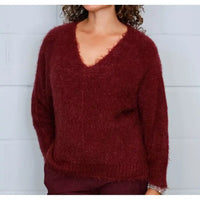 A person wearing a fuzzy, long-sleeve V-neck sweater in a deep burgundy red, standing against a light gray paneled wall.