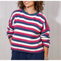 A woman wearing a fuzzy long-sleeve crewneck sweater with horizontal navy blue, white, and pink stripes, paired with navy pants.