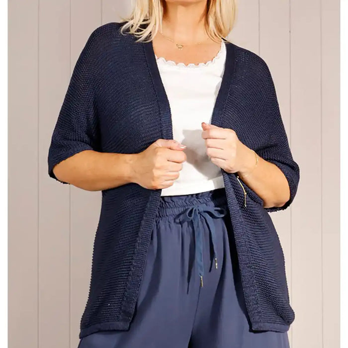 Woman wearing a navy blue cardigan and pants against a neutral background