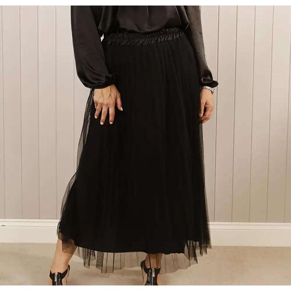 Person wearing a black dress with sheer overlay against a neutral background