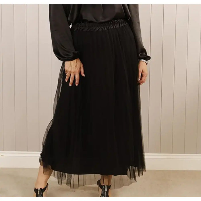 Person wearing a black dress with sheer overlay against a neutral background