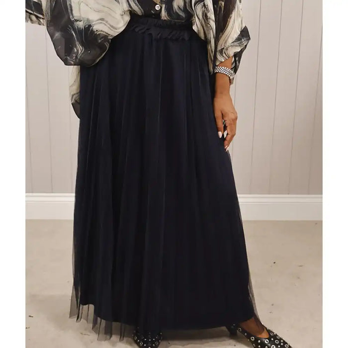 Person wearing a black skirt with a patterned top in a neutral setting