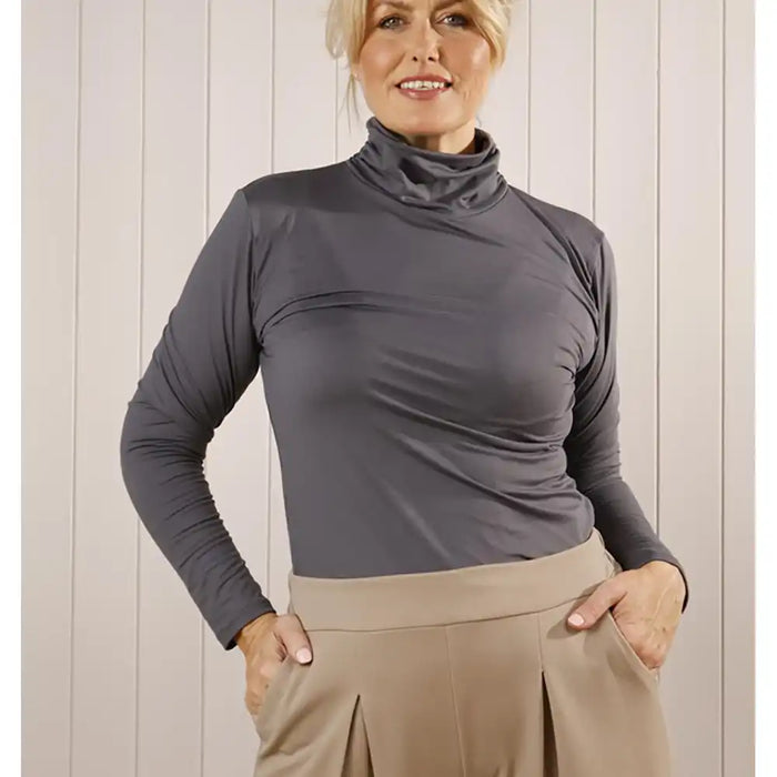 Woman wearing a gray long-sleeve top and beige pants against a light wooden panel background
