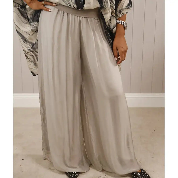 Person wearing a long, light gray skirt with a patterned top in a neutral setting.